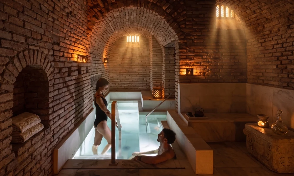 Pareja compartiendo un momento de relajación en las cálidas aguas del spa subterráneo a la luz de las velas, ideal para escapadas de parejas en Córdoba.